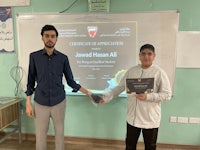 two men standing in front of a whiteboard holding a certificate