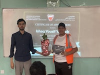 two men standing in front of a whiteboard holding a certificate